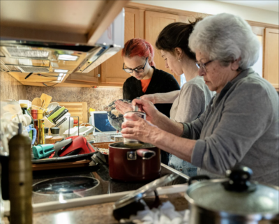 Mother, daughter, and grandmother cooking together in a small kitchen.